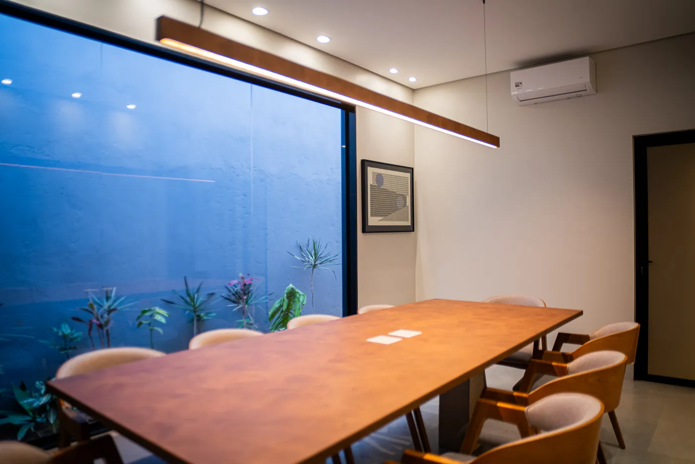 Sala de reuniões com mesa de madeira e jardim interno iluminado